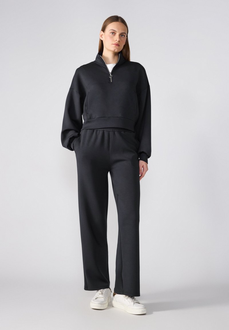 Black zip-up sweatshirt with a high collar, paired with matching loose-fit pants; both made of soft fabric with a smooth texture.
