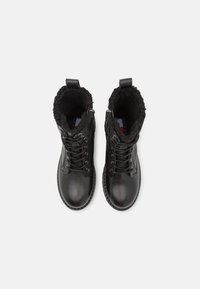 Bottines montantes à lacets en cuir noir avec doublure en fourrure et languettes de tirage, vues de dessus sur un fond blanc.