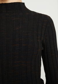 Pull noir côtelé avec un col montant, présentant de subtiles touches orange dans le tissu, une surface texturée et des manches longues ajustées.