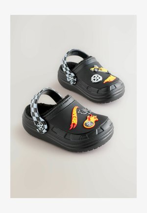 Schwarze Gummischlappen mit kariertem Riemen, verziert mit bunten Aufklebern von Autos und Flammen. Weiche Innenauskleidung für Komfort. Texturierte Sohle.