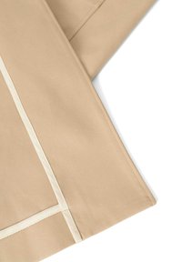 Beige Stoff mit einer glatten Textur, versehen mit einem kontrastierenden cremefarbenen Besatz entlang der Kanten und Nähte. Das Design ist minimalistisch und strukturiert.