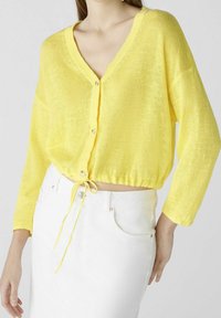 Gelbes, kurz geschnittenes Cardigan mit V-Ausschnitt, langen Ärmeln, Knopfverschluss und Kordelzug am Saum. Hergestellt aus einem leichten, strukturierten Strickmaterial.