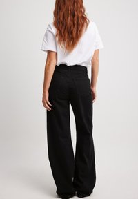 Svarta vida jeans med hög midja, med bakfickor och subtila sömnadsdetaljer. Matchas med en enkel vit t-shirt.