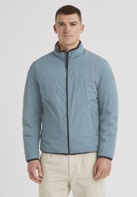 Helle blaue wasserdichte Jacke mit hohem Kragen, schwarzem Reißverschluss und Seitentaschen. Glatte Textur mit elastischen Bündchen und Saum.