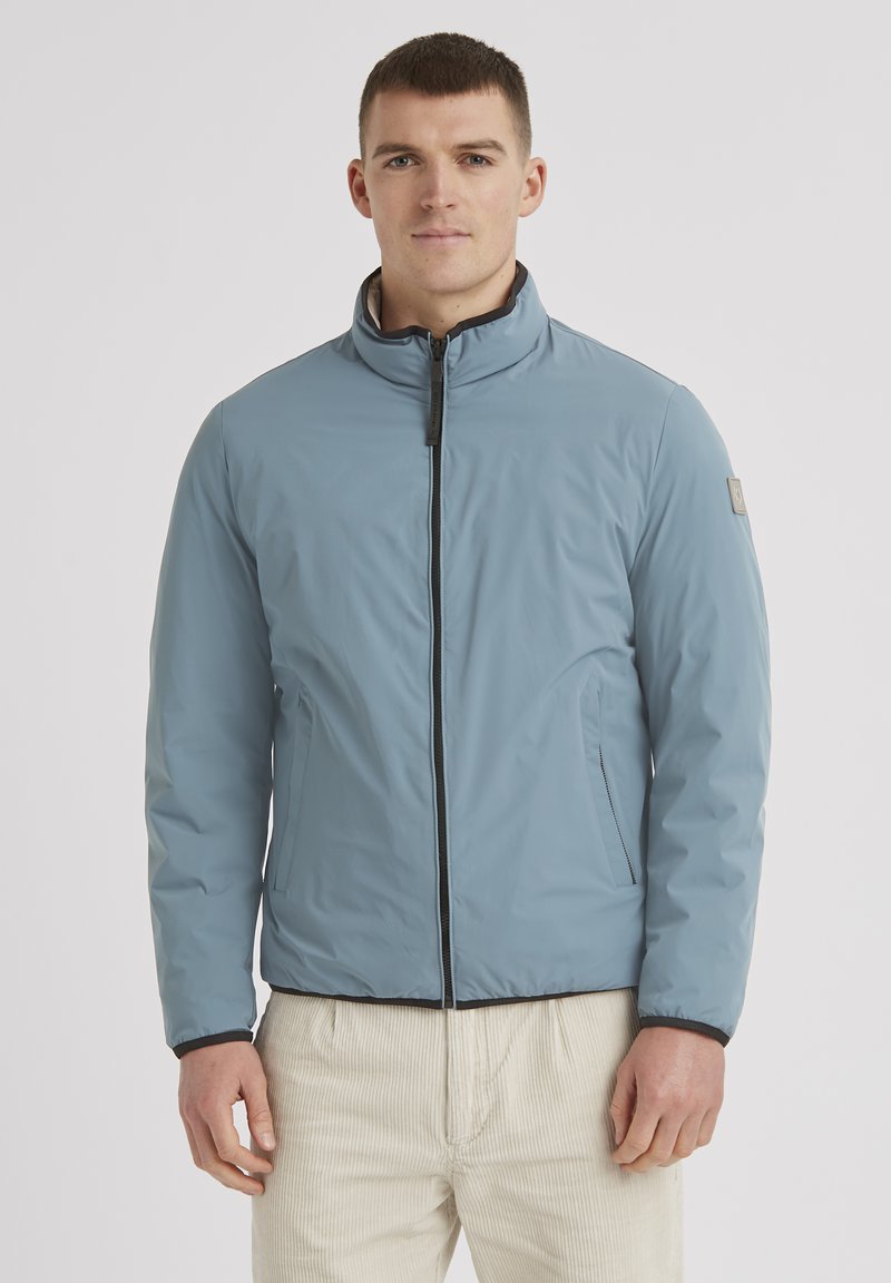 Helle blaue wasserdichte Jacke mit hohem Kragen, schwarzem Reißverschluss und Seitentaschen. Glatte Textur mit elastischen Bündchen und Saum.