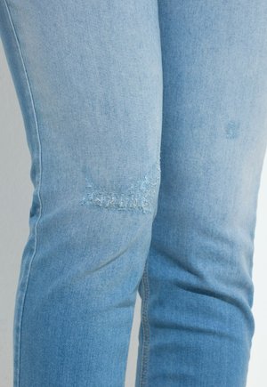 Jeans de denim azul claro con sutiles parches desgastados en la zona del muslo, primer plano que muestra la textura de la tela y los detalles de la costura.