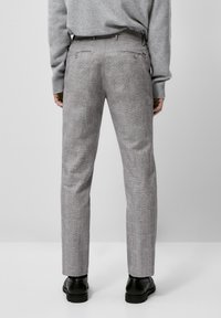 Pantaloni a quadri grigi con vestibilità slim, dotati di tasche posteriori e una trama liscia. Abbinati a un maglione grigio e scarpe nere.