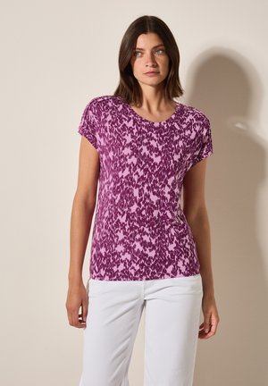 Haut à manches courtes dans un motif abstrait violet et rose, encolure ronde, tissu doux, coupe décontractée, associé à un pantalon blanc.