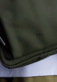 Mörkgrön vattentät väska med en slät yta och en subtil präglad "RAINS"-logotyp. Har en dragkedjestängning och rundade kanter.