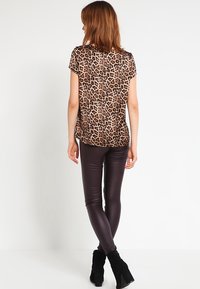 Průhledný top s leopardím potiskem a krátkými rukávy, kombinovaný s těsně padnoucími tmavě hnědými legínami a černými vysokými kotníkovými botami.