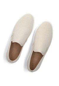 Beige canvas instappers met een witte rubberen zool, ronde neuzen en een gladde binnenvoering. Kenmerkt zich door een subtiel gebogen naad bij de opening.