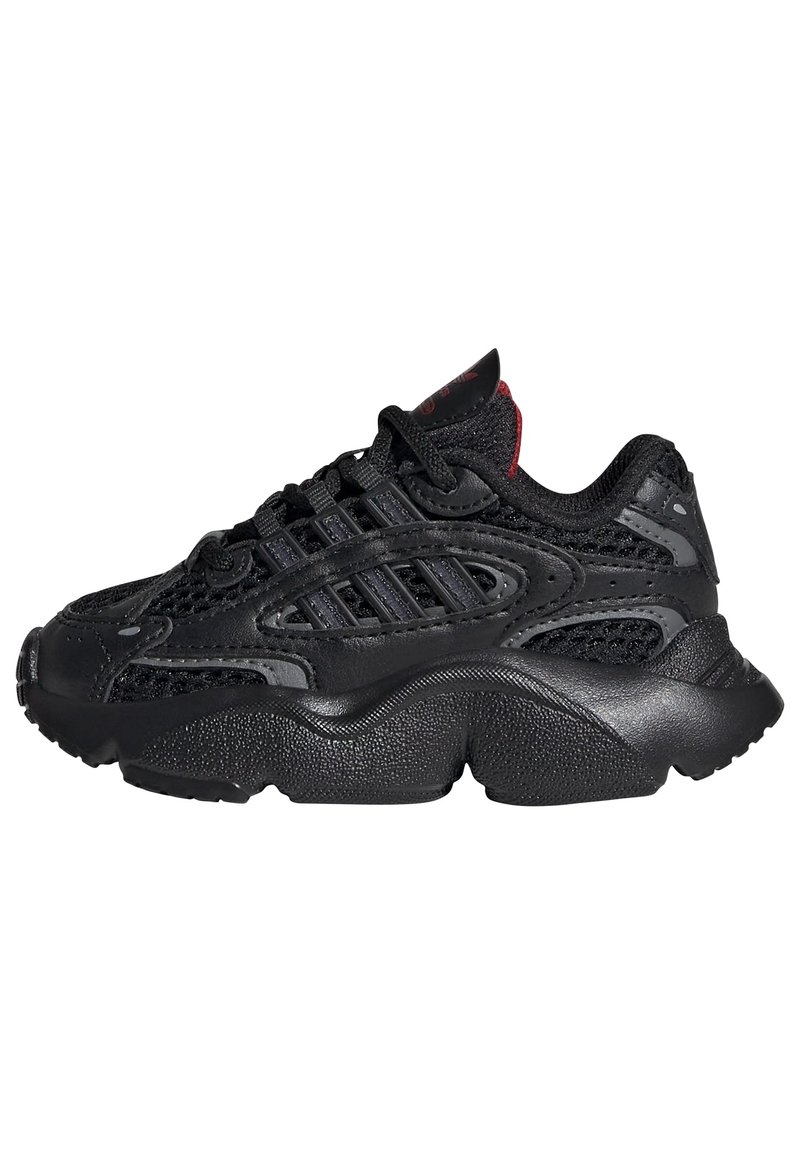 Black athletic sneakers featuring a mesh upper, textured rubber sole, and contrasting red accents on the tongue and laces.