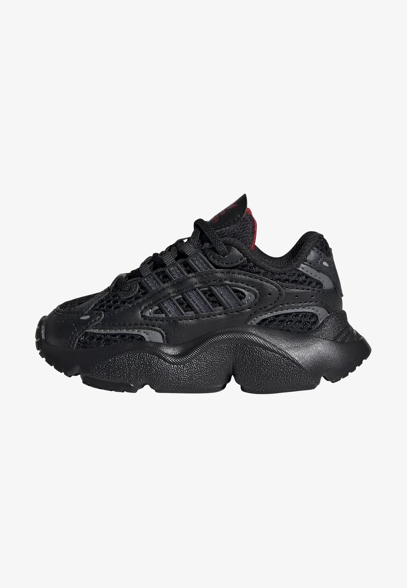 Black athletic sneakers featuring a mesh upper, textured rubber sole, and contrasting red accents on the tongue and laces.