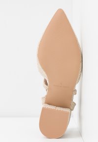 Semelle de chaussure beige à bout pointu avec talon texturé et inscription "Fabriqué en Chine", taille 4, présentée sur fond blanc.