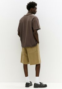 Barna, oversize póló laza szabással, khaki sorttal párosítva. Jellemzői közé tartozik az egyszínű textúra, valamint a fekete laza cipők fehér zoknikkal.