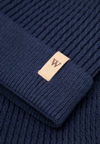 Granatowa prążkowana czapka z dzianiny o miękkiej fakturze, z naszytą jasnobrązową skórzaną metką z subtelnym logo.