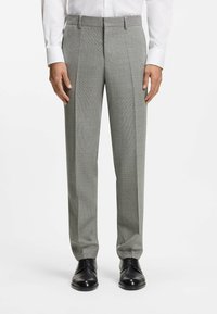 Szare, z teksturą spodnie wizytowe z przodu z zakładkami, szlufkami na pasek i dopasowanym krojem, zestawione z czarnymi eleganckimi butami.