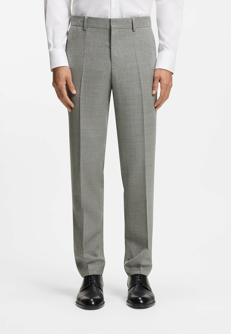 Szare, z teksturą spodnie wizytowe z przodu z zakładkami, szlufkami na pasek i dopasowanym krojem, zestawione z czarnymi eleganckimi butami.