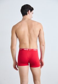 Rote Baumwoll-Boxershorts mit einem weißen Nike-Logo am Bund, die eine enganliegende Passform und eine glatte Textur aufweisen. Modell von hinten gezeigt.