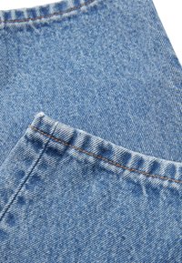 Primer plano de tela de mezclilla azul, con un bolsillo y costuras naranjas, que muestra una textura suave y un sutil patrón desvaído.