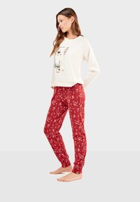 Haut long beige clair avec un graphique de hibou ; pantalon de pyjama rouge avec des imprimés d'animaux et de la nature. Tissu doux avec une coupe décontractée.