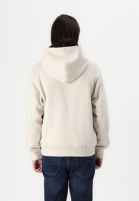 Beige hoodie with a large hood, kangaroo pocket, ribbed cuffs, and hem. Worn with dark denim jeans; soft material and relaxed fit.