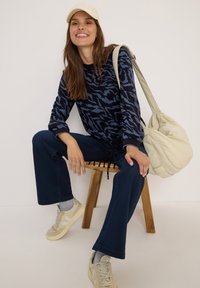 Mörkblåmönstrad tröja med långa ärmar, kombinerad med mörkblå vida byxor och beiga sneakers, accessoriserad med en ljus väska.
