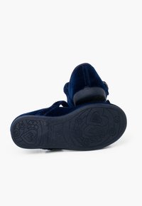 Zapato de terciopelo azul marino con correa ajustable, punta redonda y suela de goma texturizada que presenta patrones florales y acentos de corazón.