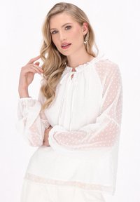 Weiße Bluse mit strukturierten Punkten, hohem Rüschenausschnitt und elastischen Manschetten. Durchscheinendes Material mit langen Ärmeln und lockerer Passform.