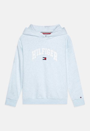 Lyseblå hettegenser laget av mykt stoff med logo foran, har snøring i hetten og ribbede mansjetter, og er akkuert med et lite rødt, hvitt og blått merke.