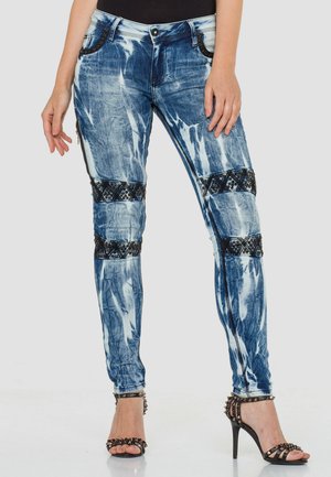 Blaue Batik-Skinny-Jeans mit strukturierten schwarzen Musterelementen an den Knien, ausgestattet mit Fronttaschen und einem Reißverschlussdetail an der Seite.