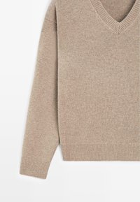 Maglione beige lavorato a maglia con scollo a v, maniche lunghe e polsini a coste. Il tessuto appare morbido con una leggera texture.