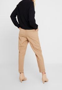 Pantaloni beige su misura con tasche laterali e risvolti, abbinati a un maglione nero a trama e stivaletti color nudo con tacco basso.