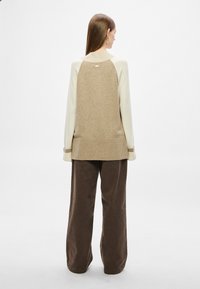 Πλεκτό πουλόβερ σε μπεζ και κρεμ αποχρώσεις, με ριμπ τελείωμα και μανσέτες. Χαλαρή γραμμή, με μικρή ετικέτα λογότυπου στο πίσω μέρος του λαιμού.