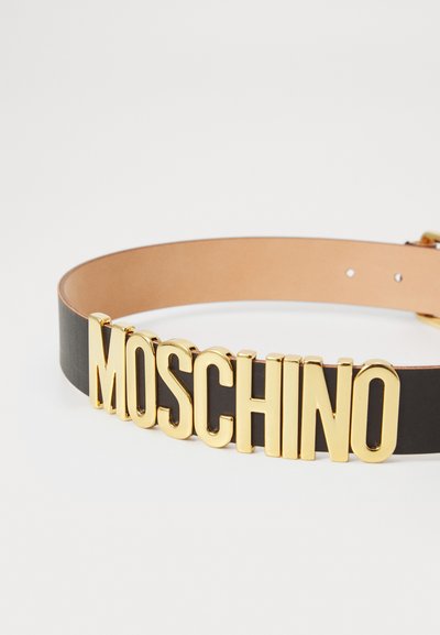 Black leather belt with large gold letters spelling "MOSCHINO" across the front on a white background.