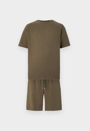 Rövid ujjú, olívazöld kerek nyakú póló, hozzáillő, rugalmas derékpántos, húzózsinóros rövidnadrággal, egyszínű háttér előtt.