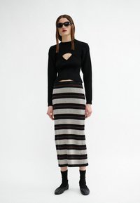 Schwarzes, geripptes Langarmshirt mit einem ausgeschnittenen Ausschnitt, kombiniert mit einem gestreiften Midirock in Beige, Schwarz und Bordeauxrot. Schwarze Ballerinas.