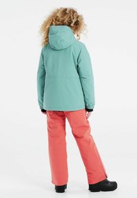 Veste imperméable turquoise avec капuche, associée à un pantalon imperméable corail. Des bottes noires complètent la tenue. Design simple, fonctionnel.