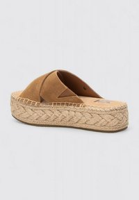 Sandalias deslizantes de ante marrón con base de yute tejido, que presentan un diseño de espadrille y parte superior con tiras cruzadas. Punta redondeada y suela plana.