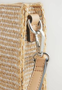Bolso de paja tejido con un acabado texturizado, detalles en plata y una correa de cuero marrón con un cierre metálico.