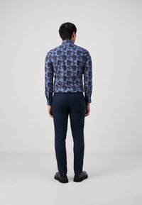 Blå mönstrad skjorta med blommönster, långa ärmar och figursydd form, i kombination med mörka byxor och svarta skor. Ren, modern look.