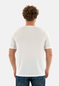 Camiseta blanca de manga corta, hecha de una tela suave con un cuello redondo. Diseño simple, con un pequeño logo en la parte superior de la espalda.