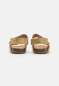 Gule lær sandaler med to justerbare stropper, korkfotbed og gummisåle. Bakfra med fokus på stroppe tekstur og materialdetaljer.