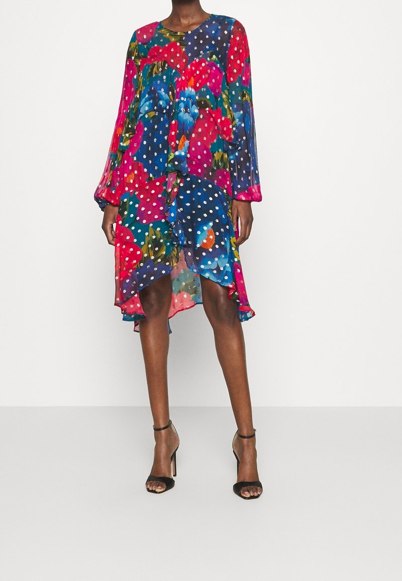 Květinové šaty s velkými červenými a modrými květy a puntíkovým vzorem. Vyrobené z lehké látky, s dlouhými rukávy a splývavým střihem.