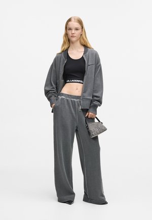 Grå velour tracksuit med en lynlåsjakke og brede bukser, parret med en sort cropped top og en lille mønstret håndtaske.