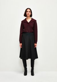 Top a maglia bordeaux con ampio colletto e un bottone, abbinato a una gonna nera a trapezio e stivali neri in pelle al ginocchio.