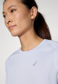 Svijetloplava sportska majica s okruglim izrezom, koja na prsima ima suptilni logotip i teksturiranu tkaninu, prikazana na gornjem dijelu tijela modela.