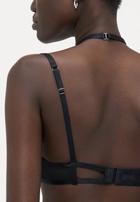 Lingerie nera con spalline in satin regolabili, chiusura a gancio e occhiello e una superficie liscia opaca, che mette in mostra un design minimalista.