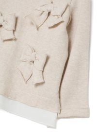 Beige gebreide stof met drie genaaide strikken en een witte laagjeszoom, die een deel van een lange mouw garen laat zien.