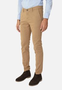 Chinos in cotone beige con vestibilità slim, dotati di chiusura a bottone, tasche laterali e risvolti, abbinati a stivali in suede marrone scuro.
